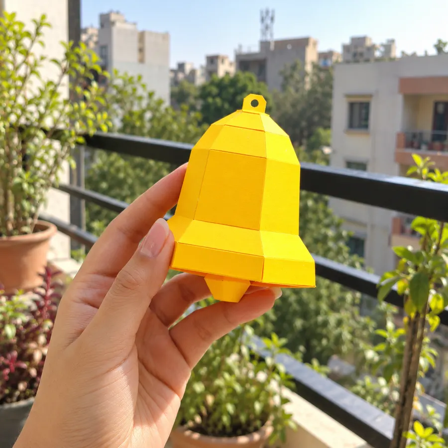 A hand holding a yellow paper bell on a sunny balcony