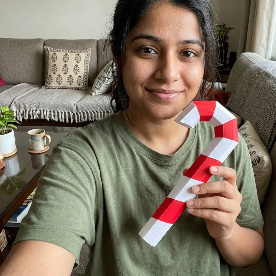 A woman smiling on a sofa holding a red and white paper candy cane