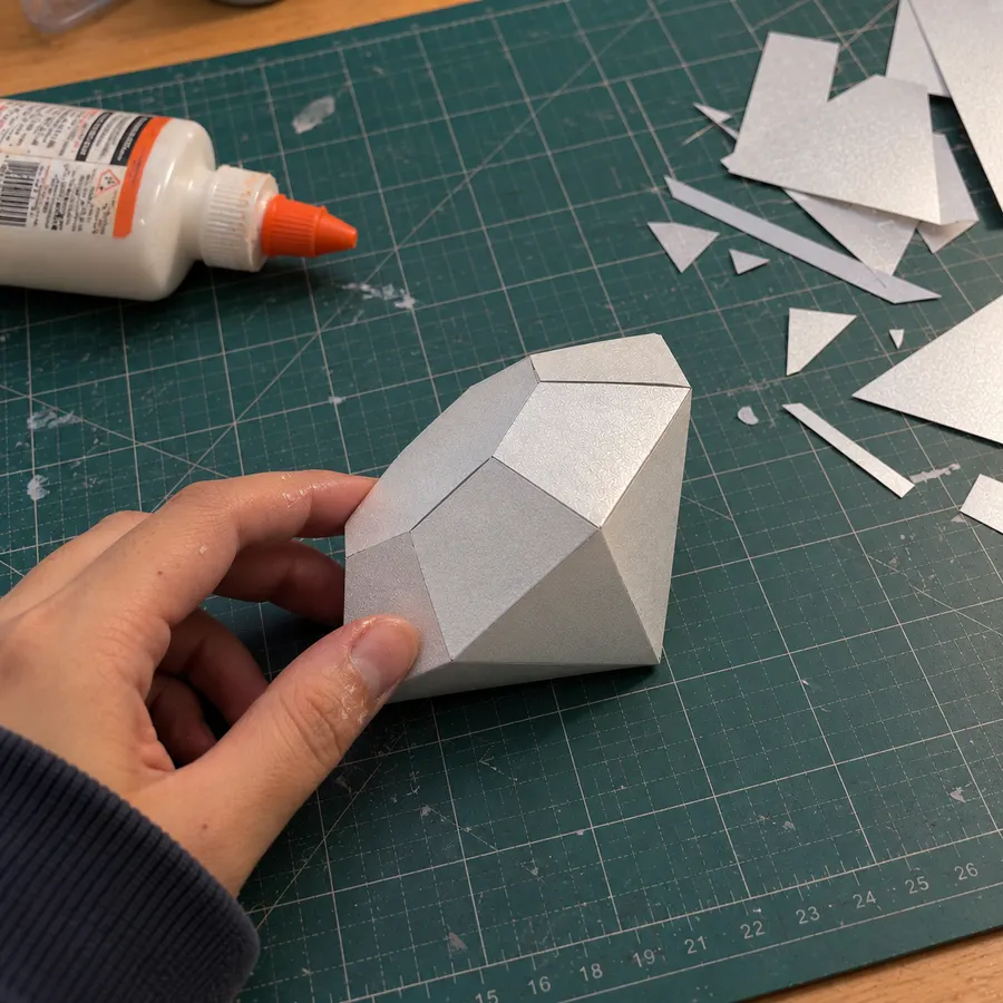 A silver paper diamond on a cutting mat next to glue and paper scraps