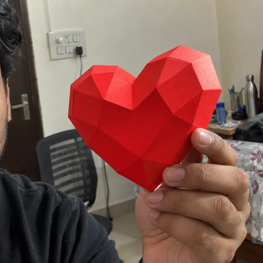 A man holding a red paper heart close to the camera