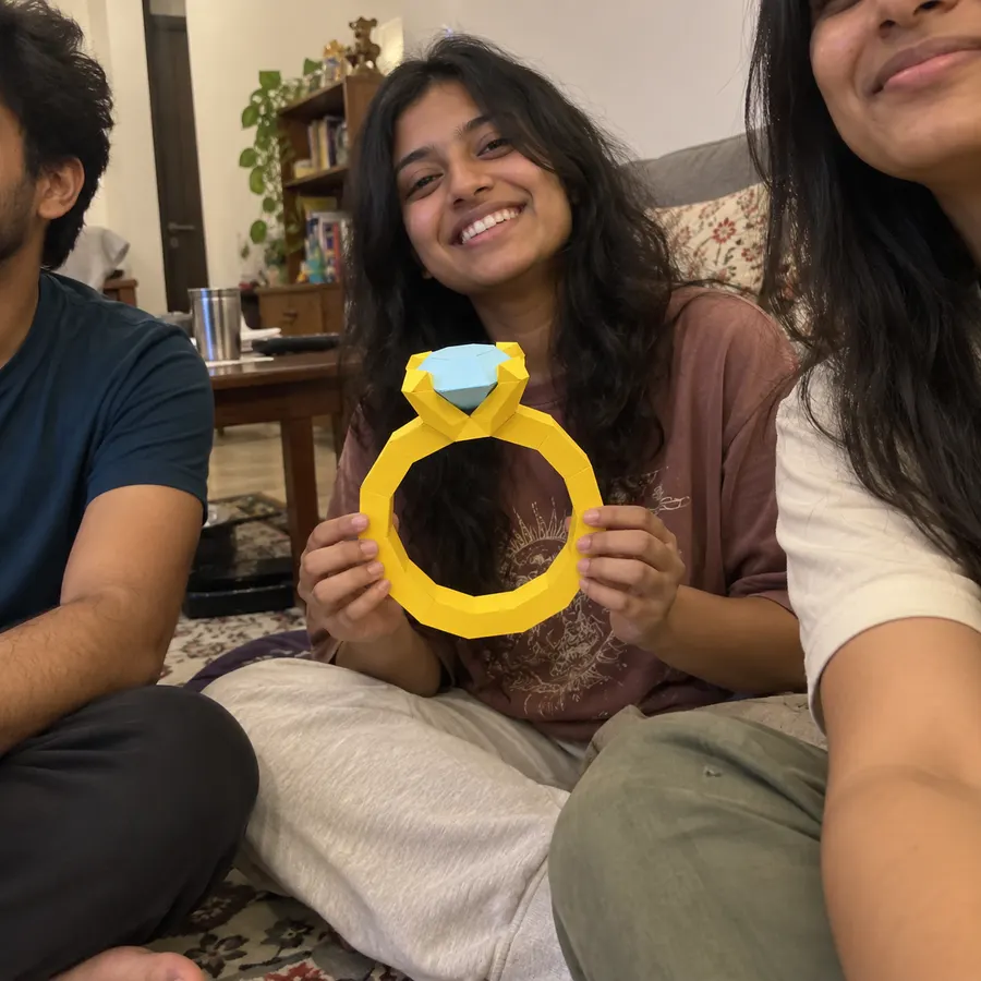 A smiling woman holding a big yellow paper ring with a blue gem, friends beside her