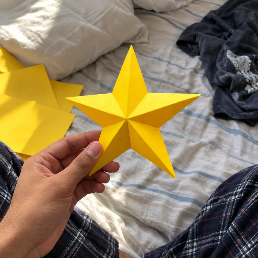 A hand holding a yellow paper star over a bed