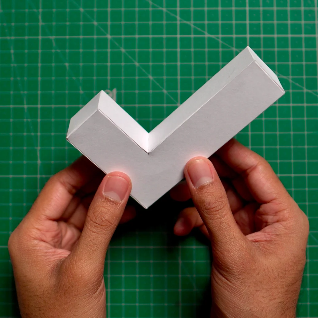 The finished paper check mark, glued together, held in two hands