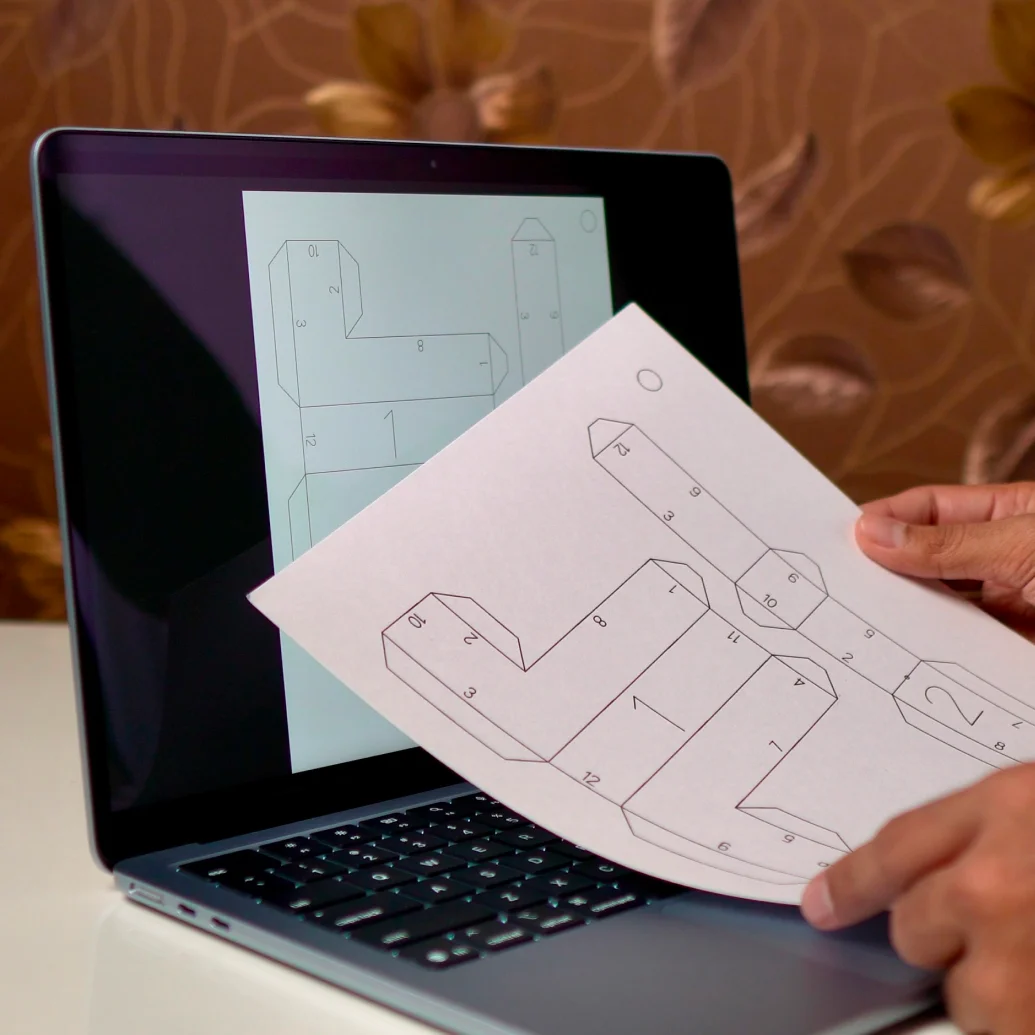 A freshly printed pattern held up in front of a laptop showing the same pattern