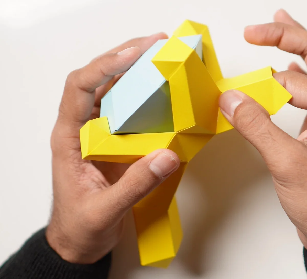 Hands pressing the folded yellow prongs of the paper ring around its blue diamond